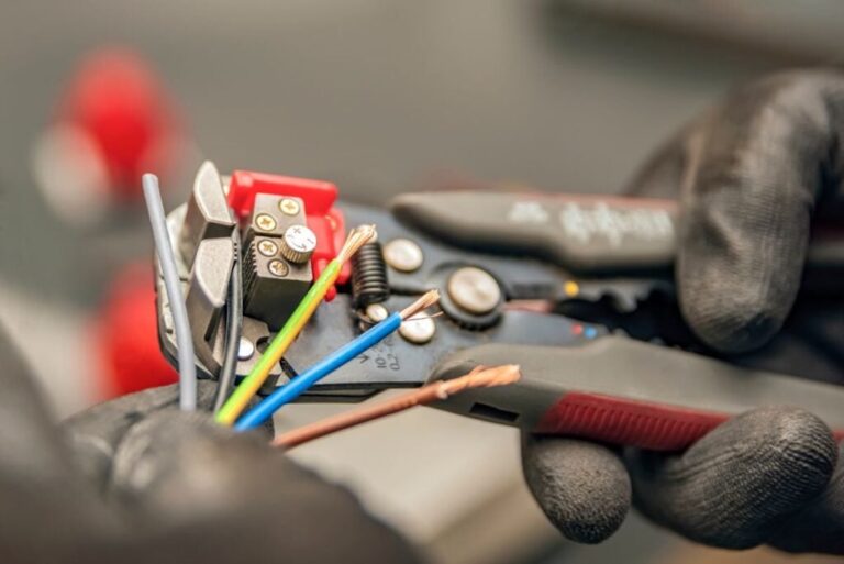 The electrician cleans the protective insulation from the wire using a wire stripper