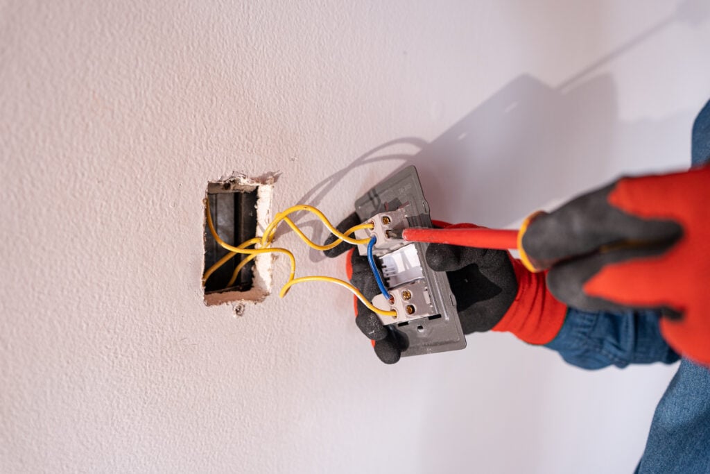 Close-up of an experienced electrician's hands repairing a breaker with a screwdriver