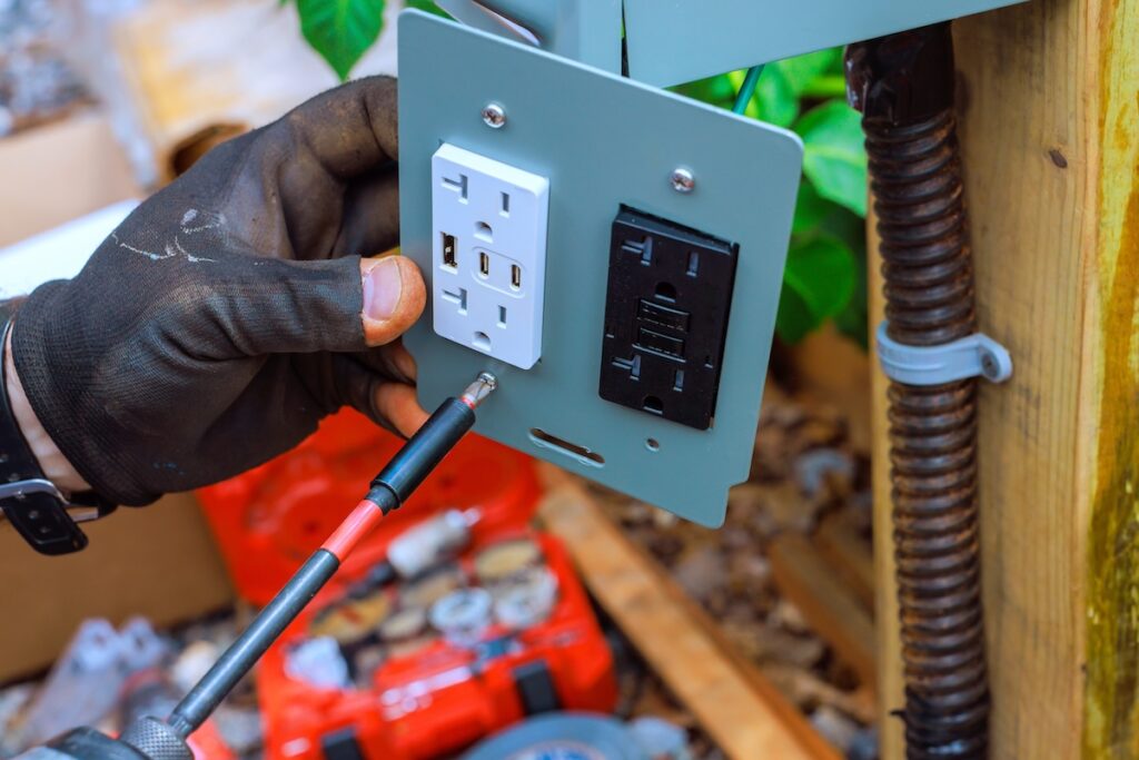 Worker is using screwdriver to install an electrical outlet with USB ports on wooden post outdoors. 