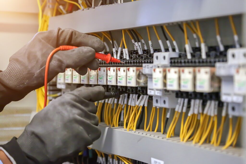 Electrical engineer using digital multimeter to check current voltage at circuit breaker in main distribution board.