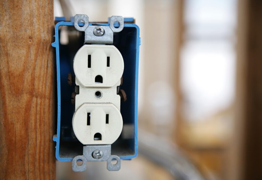 A 120v duplex electrical receptactle box nailed to a wooden stud.  